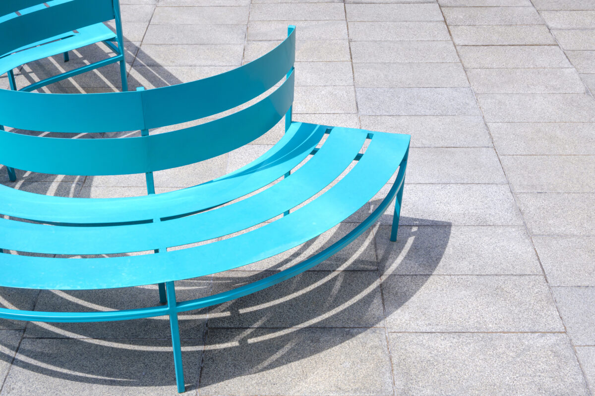 Blue semi circular metal bench on gray marble tile floor in public park area