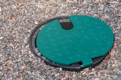 A plastic hatch in the garden covering the connection point for the irrigation hose. A protective hatch in the garden for connecting water and watering plants.