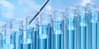 Test tubes filled with blue liquid. A pipette is dispensing a droplet.